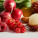Uma variedade de frutas frescas que começam com a letra R, incluindo framboesas, rabanetes, groselhas vermelhas e rambutan, dispostas sobre uma superfície branca.